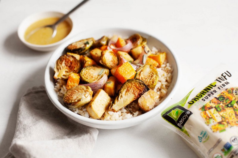 A block of extra firm tofu is perched next to a bowl of roasted tofu and vegetables, along with a small pinch pot of dressing.