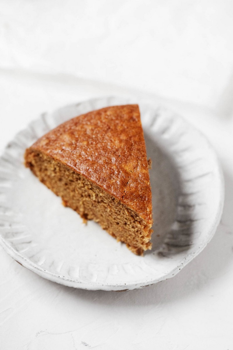 A golden brown slice of vegan gingerbread cake is laid out on a small dessert plate.