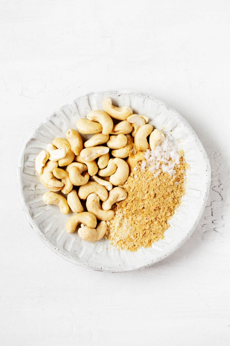 A small porcelain plate holds raw cashews and nutritional yeast.