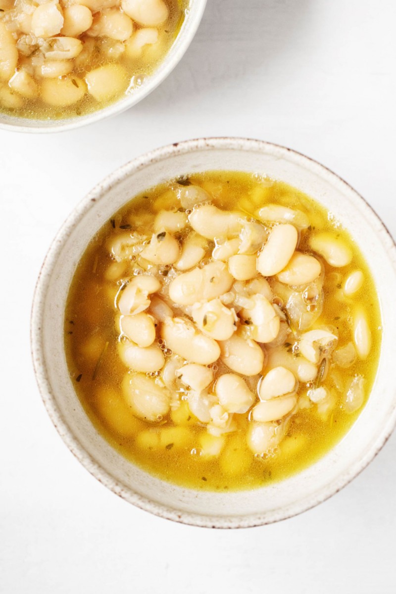 Two ceramic bowls have each been filled with a cooked batch of legumes. 