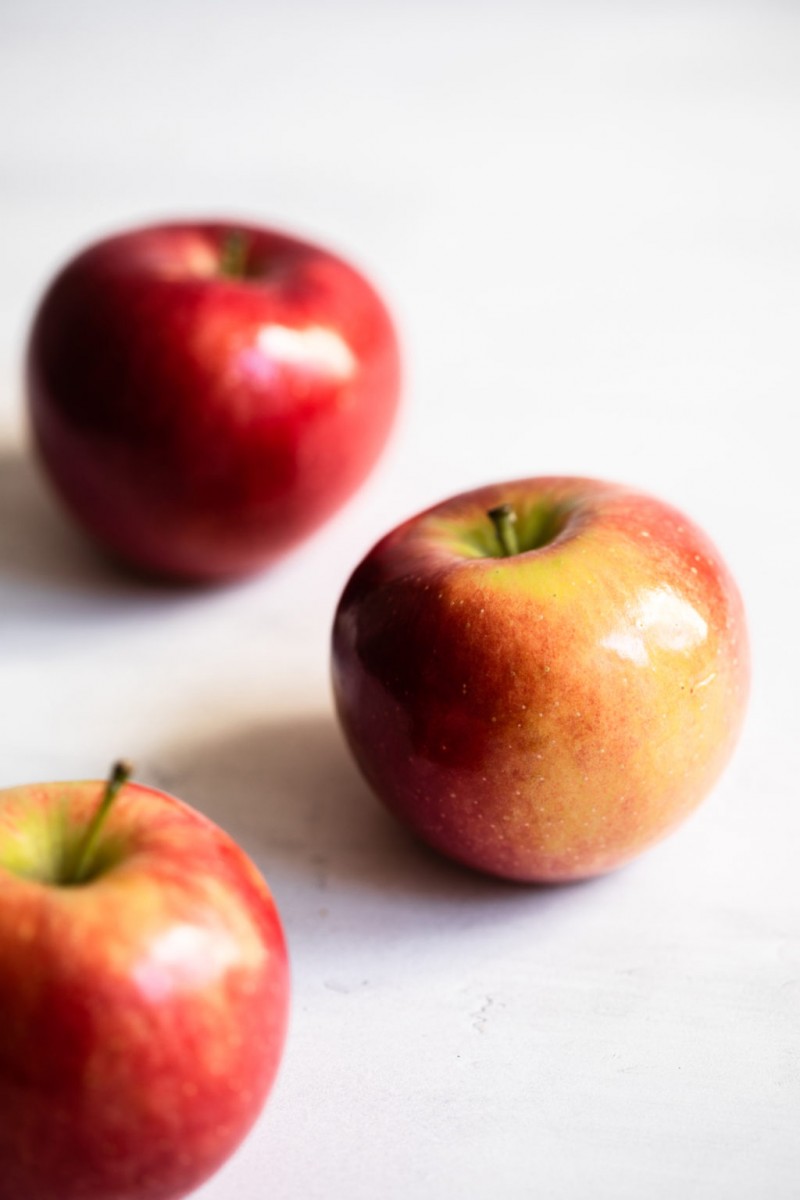 A photograph of three crimson red and golden apples on a bright, white backdrop.