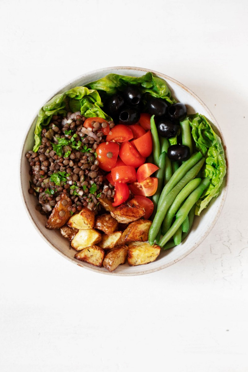 An overhead image of a bowl of plant-based salad, which has been made with green beans, tomatoes, olives, and butter lettuces.