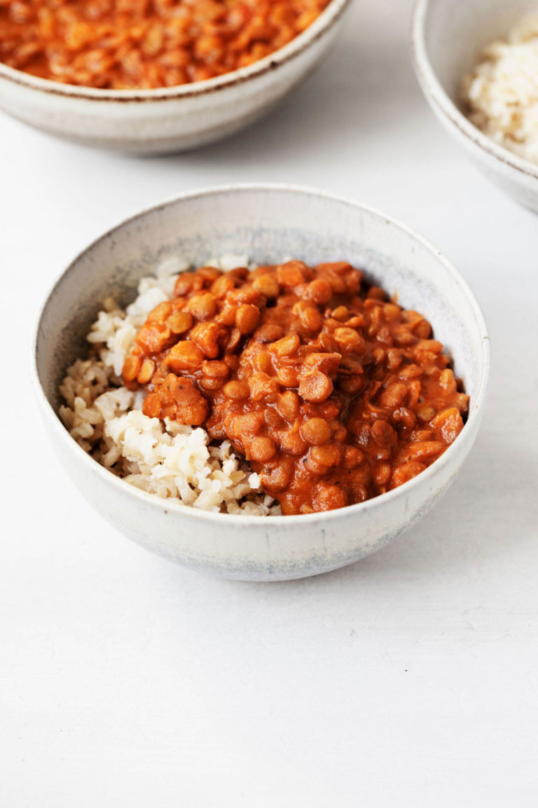 Two white, ceramic bowls hold dishes of masala spiced lentils and cooked brown rice.