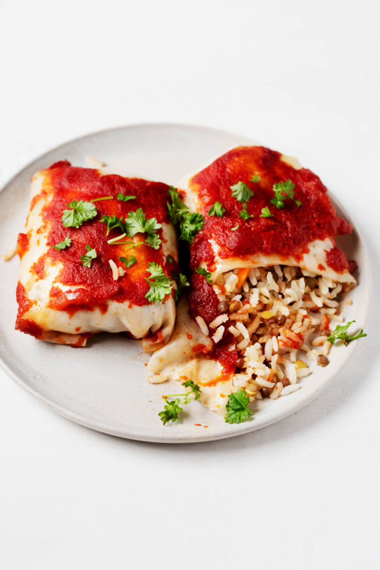 Two stuffed cabbage rolls are laid out, side by side, on a plate. One has been cut into and the filling is spilling out.