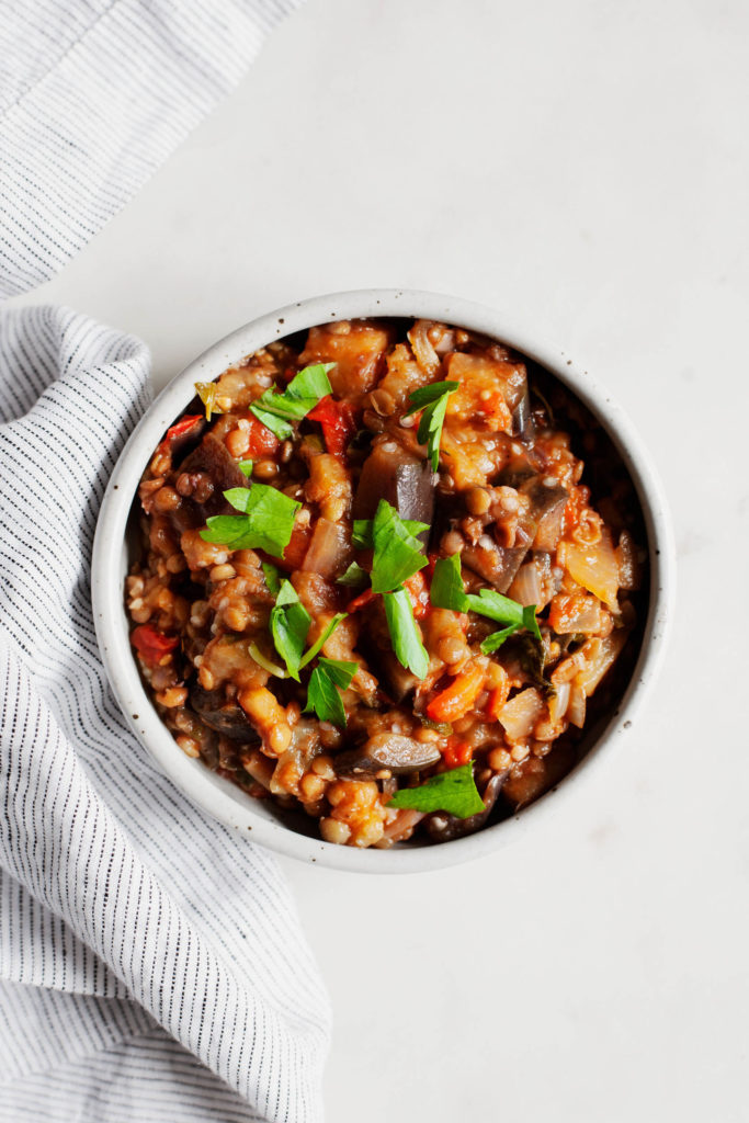 An overhead shot of stewed eggplant tomato lentils, garnished with parsley and basil.