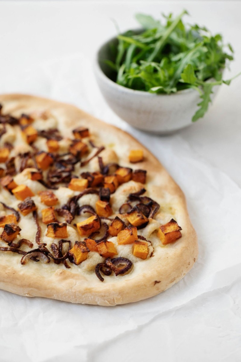 A butternut squash and red onion pizza, just baked and about to be sprinkled with fresh, green baby arugula.