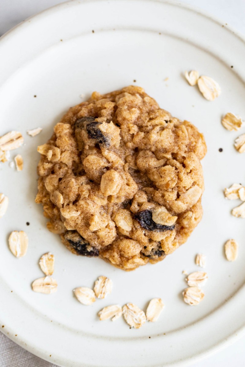 A single, chewy oatmeal raisin cookie rests on a white plate.