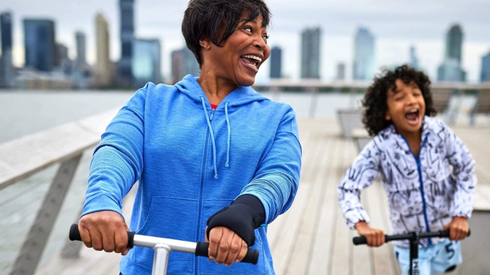 A woman wears a black wrist brace and rides a scooter alongside her daughter.