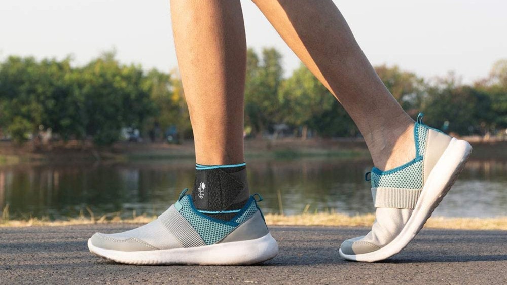 A person wearing a black and blue ankle brace and silver sneakers walks by a pond.