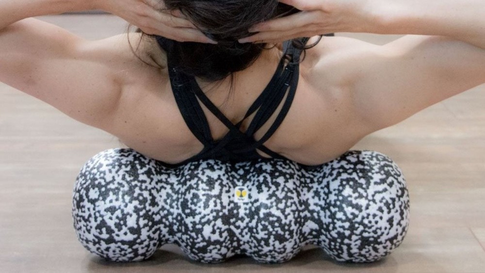 A woman using a foam roller on her upper back. 