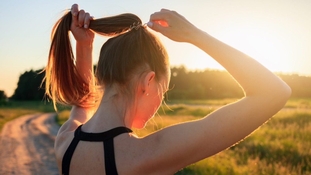 A woman puts her hair in a pony tail while outside.