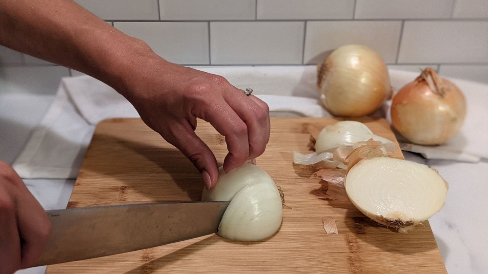 Slicing an onion multiple times vertically with a few onions and peels in the background.