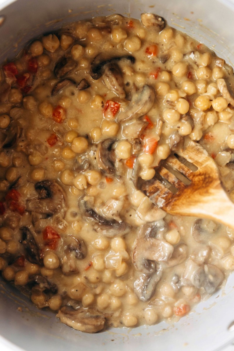 A dish of mushrooms and beans is simmering in a skillet. Dots of red pepper are distributed through the dish.