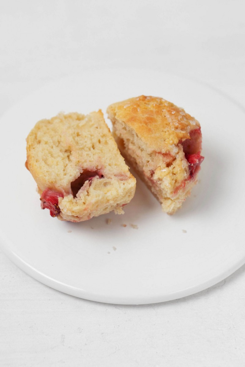 A freshly baked muffin has been broken into two halves. It's resting on a small white serving plate.