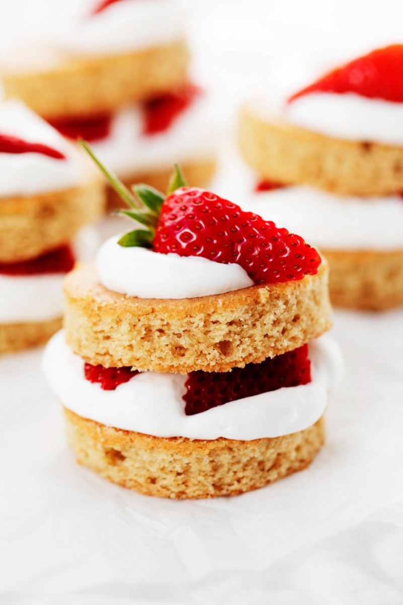 Two layers of vegan vanilla cake have been turned into strawberry shortcake, decorated with whipped cream and quartered strawberries.