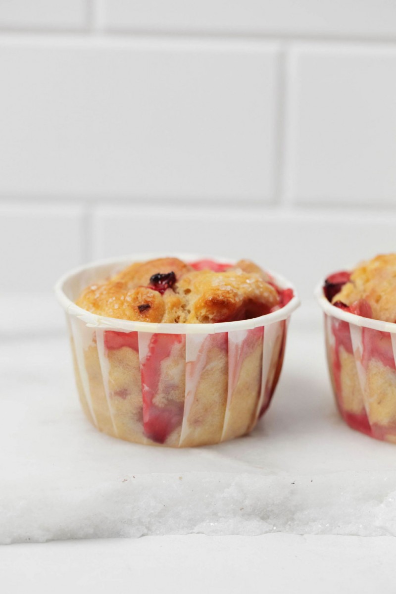 Freshly baked breakfast goods are lined up on a white marble surface, against a white tile backdrop. They're studded with seasonal berries.