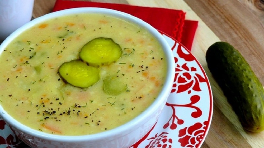 A bowl of dill pickle soup garnished with fresh dill, cracked pepper and a few pickle chips. 