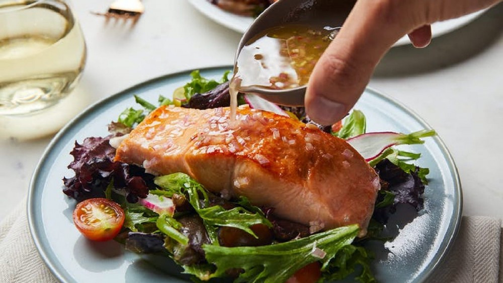 An image of a salmon salad being topped with a housemade pickle brine vinaigrette. 