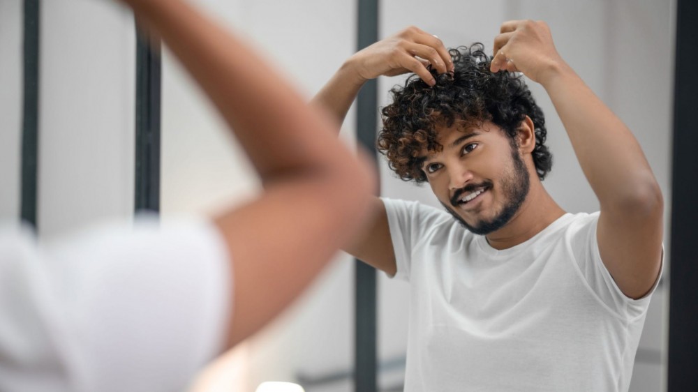 Guy with curly hair putting in hair mousse.