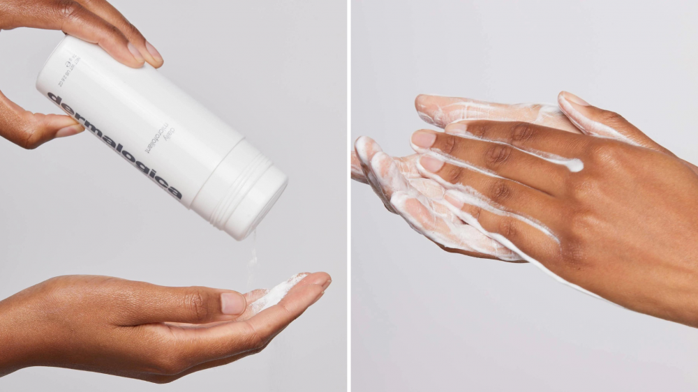 A person places powdered exfoliant into their palm, and a person lathers powder with water to create a foam.