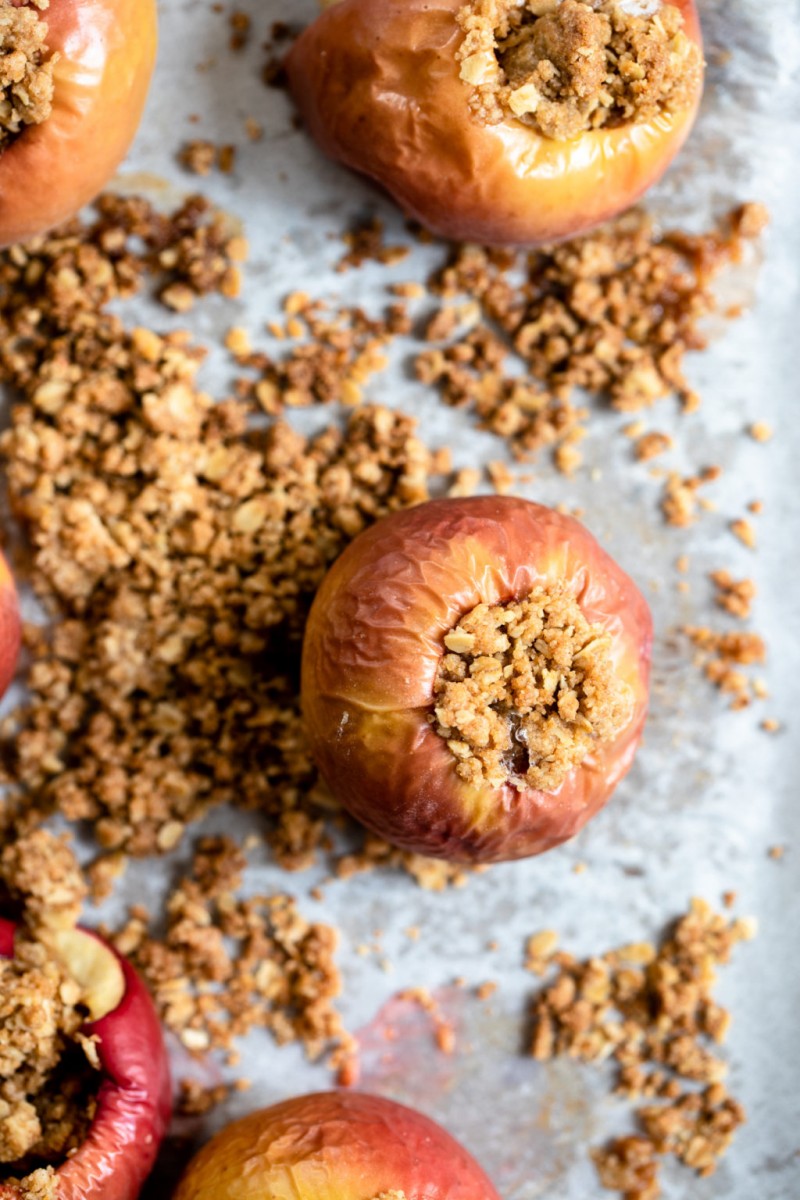 An overhead photograph of baked, stuffed apples, which are still resting on a parchment-lined baking sheet.