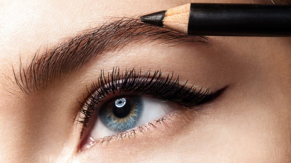 Closeup of an eye and eyebrow with a brown eyebrow pencil filling in the brow.