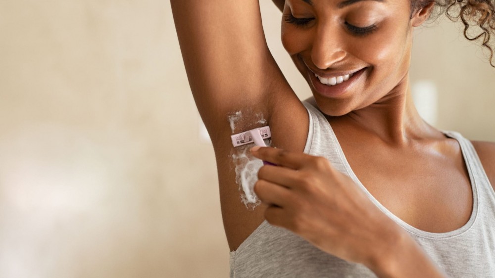 Young African American woman shaving armpits in bathroom.