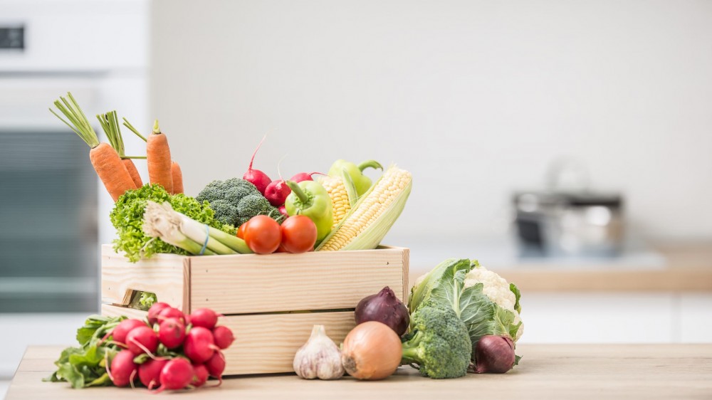 A group of various produce is arranged in a wooden basket on a kitchen counter.