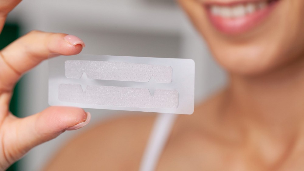 Woman holding teeth whitening strips.