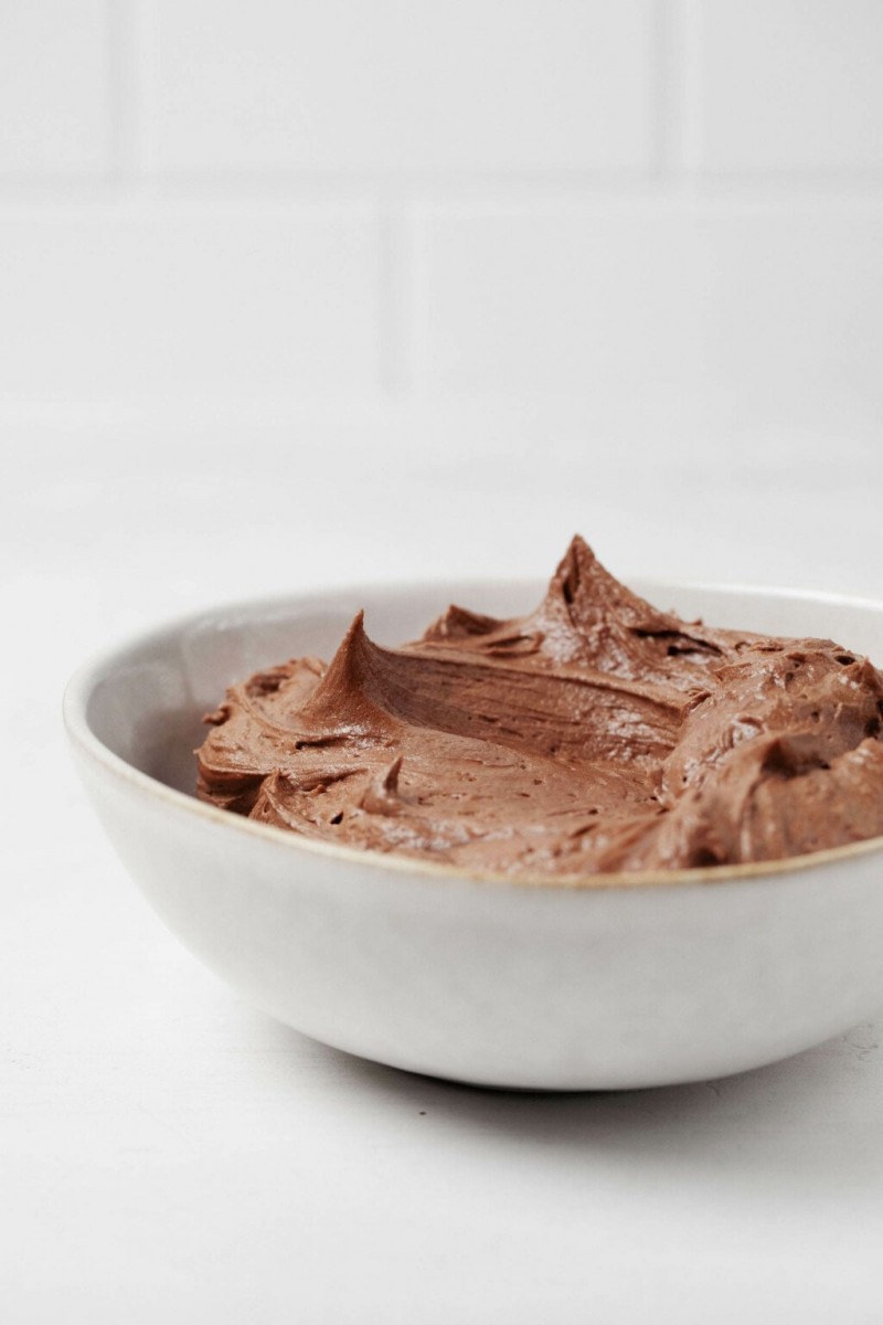 A round, ceramic, pale white gray bowl has been used to hold a rich buttercream icing.