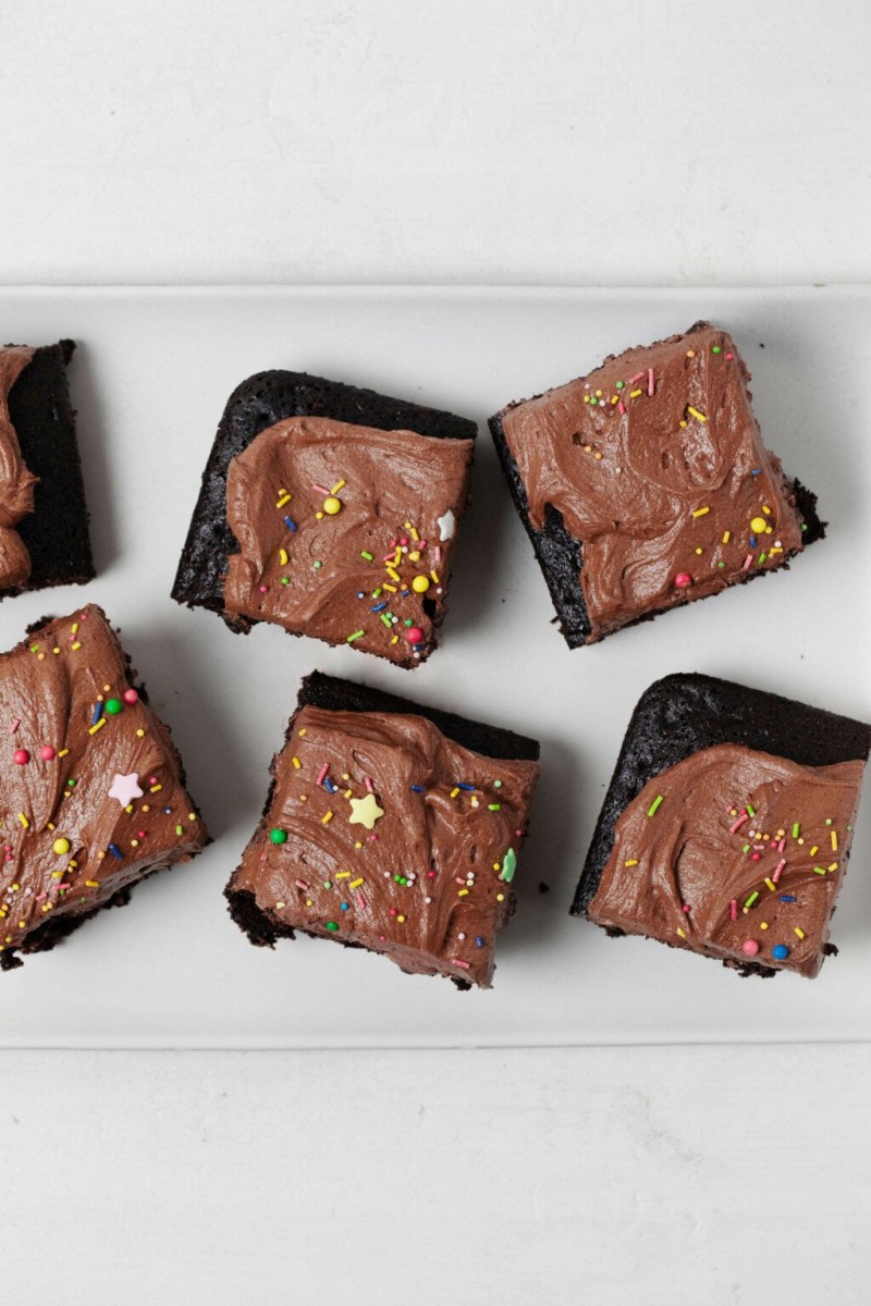 Frosted squares of a snack cake are laid out on a white platter. Each square is topped with decorative sprinkles.