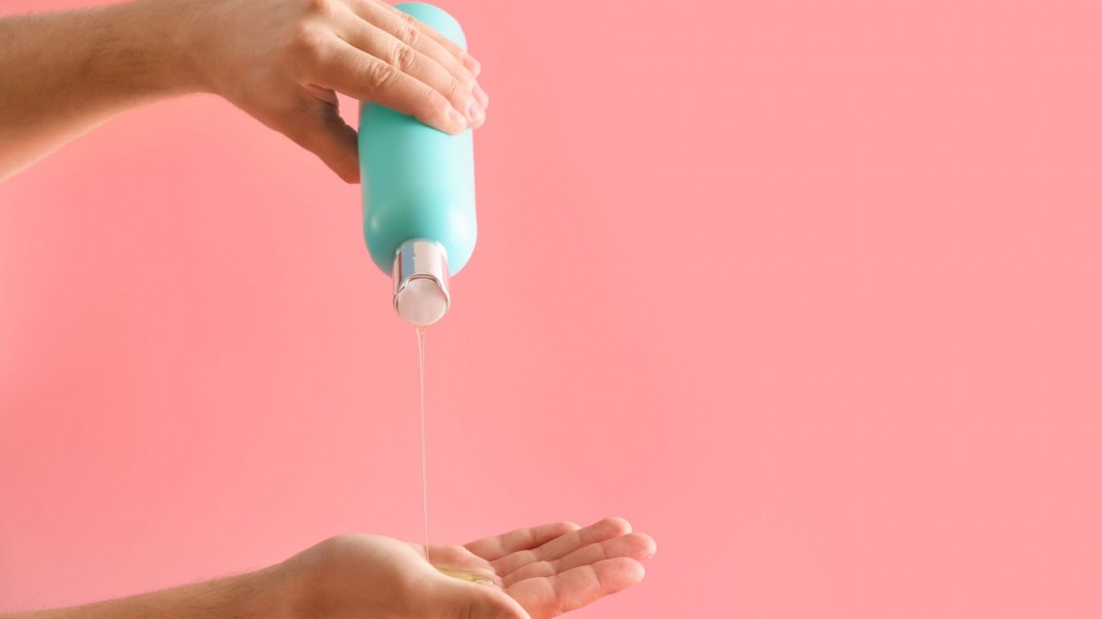 A pair of hands squeezing out shampoo from a bottle.