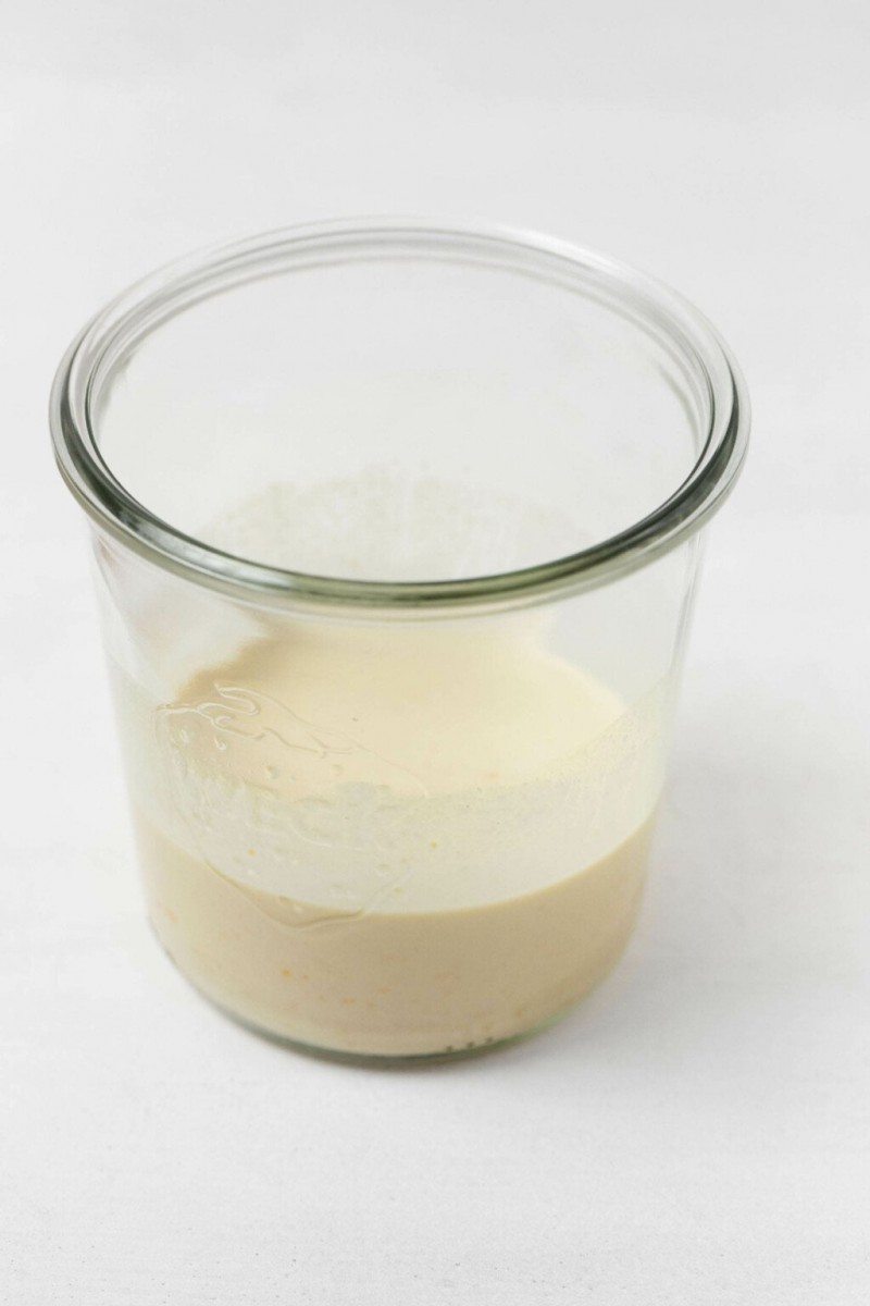 An overhead image of a creamy, off-white orange tahini dressing, which has been poured into a glass mason jar.