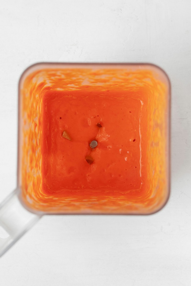 A red, creamy sauce has just been blended in a blender.