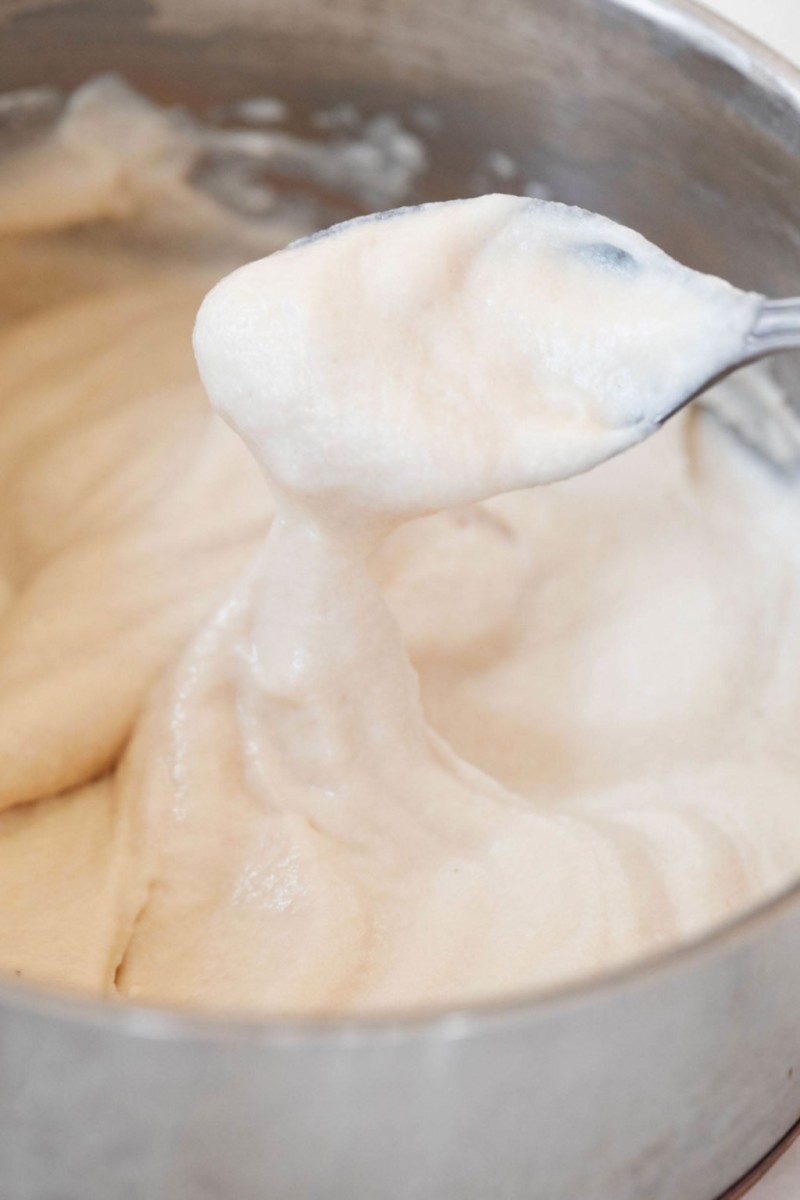 A close up image of a spoon that is covered in a rich, white, melty vegan cashew mozzarella cheese sauce.