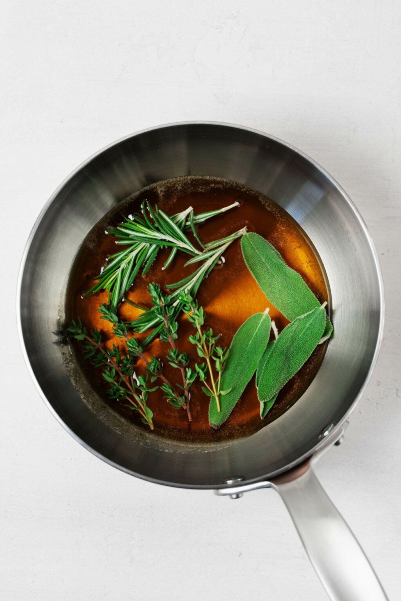 A metal saucepan is filled with syrup and fresh, bright green herbs.