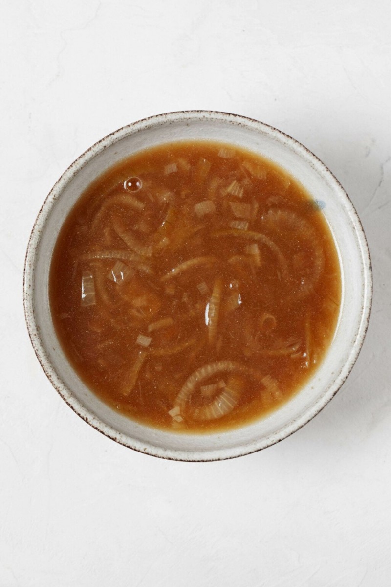 An overhead image of a bowl of brown onion soup in a white ceramic bowl. 