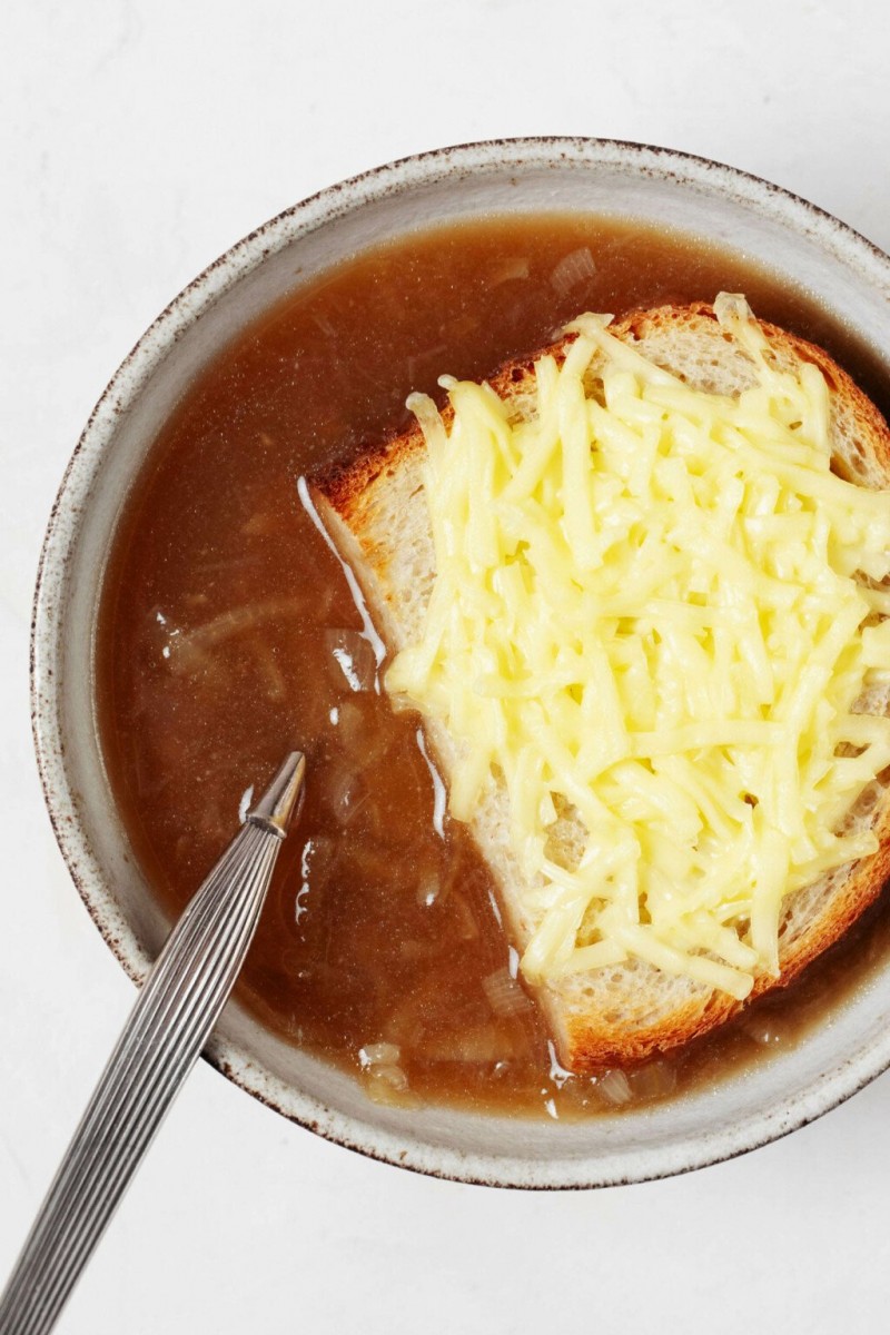 An overhead image of a bowl of French onion soup. A spoon rests in the soup.