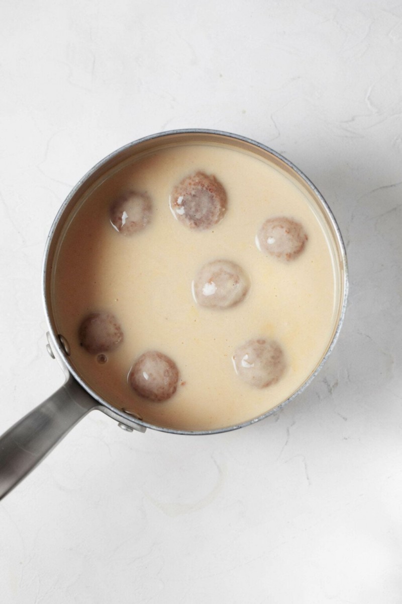 A small, silver sauce pan is pictured from above. It's filled with a creamy sauce and plant-based meatballs.