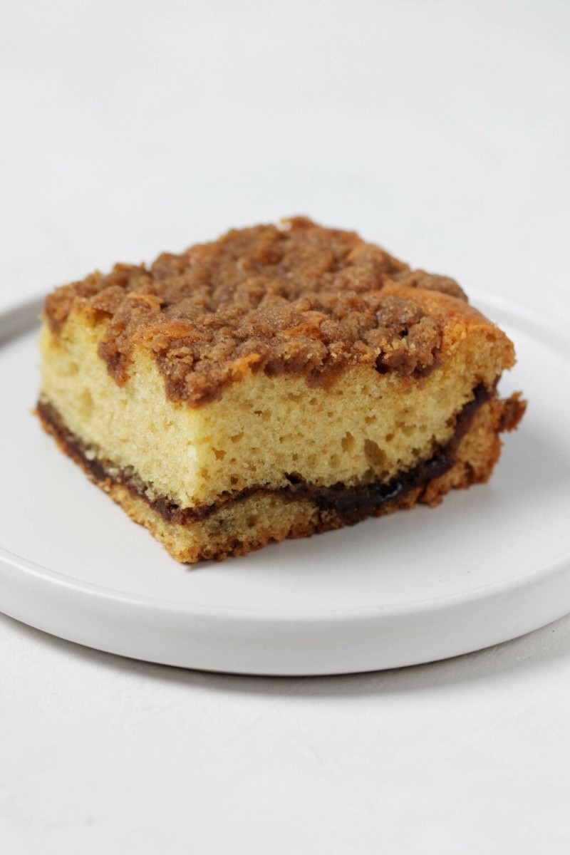 An angled photograph of a slice of vegan sour cream coffee cake, with a ribbon of cinnamon filling and streusel topping.