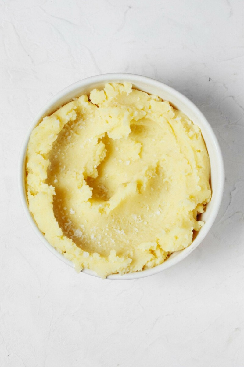 An overhead image of a white bowl, filled with fluffy vegan mashed potatoes.