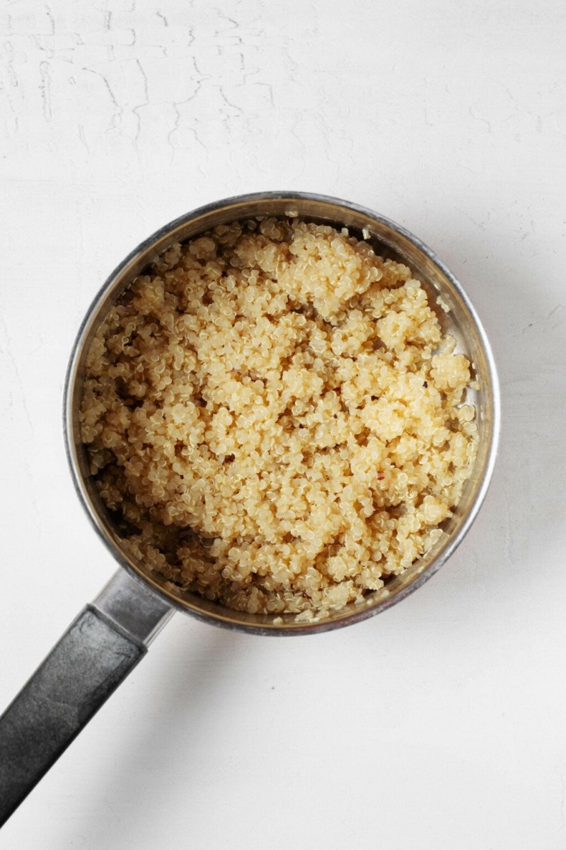 An overhead image of a silver saucepan, which is filled with fluffy, cooked quinoa.