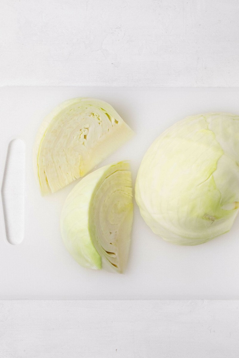 A small head of green cabbage is being cut on a white cutting board.