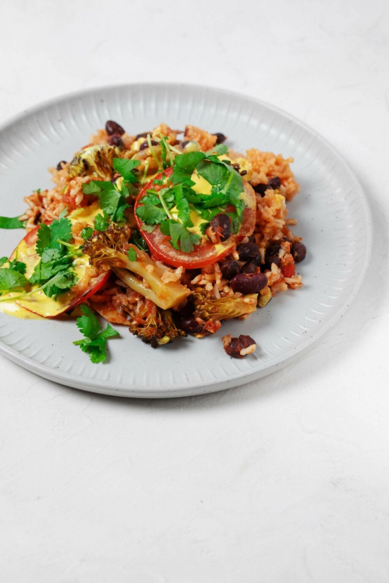 A photo of a round, grayish white plate, which has been topped by a bean and brown rice casserole. Green cilantro leaves are garnished on top.