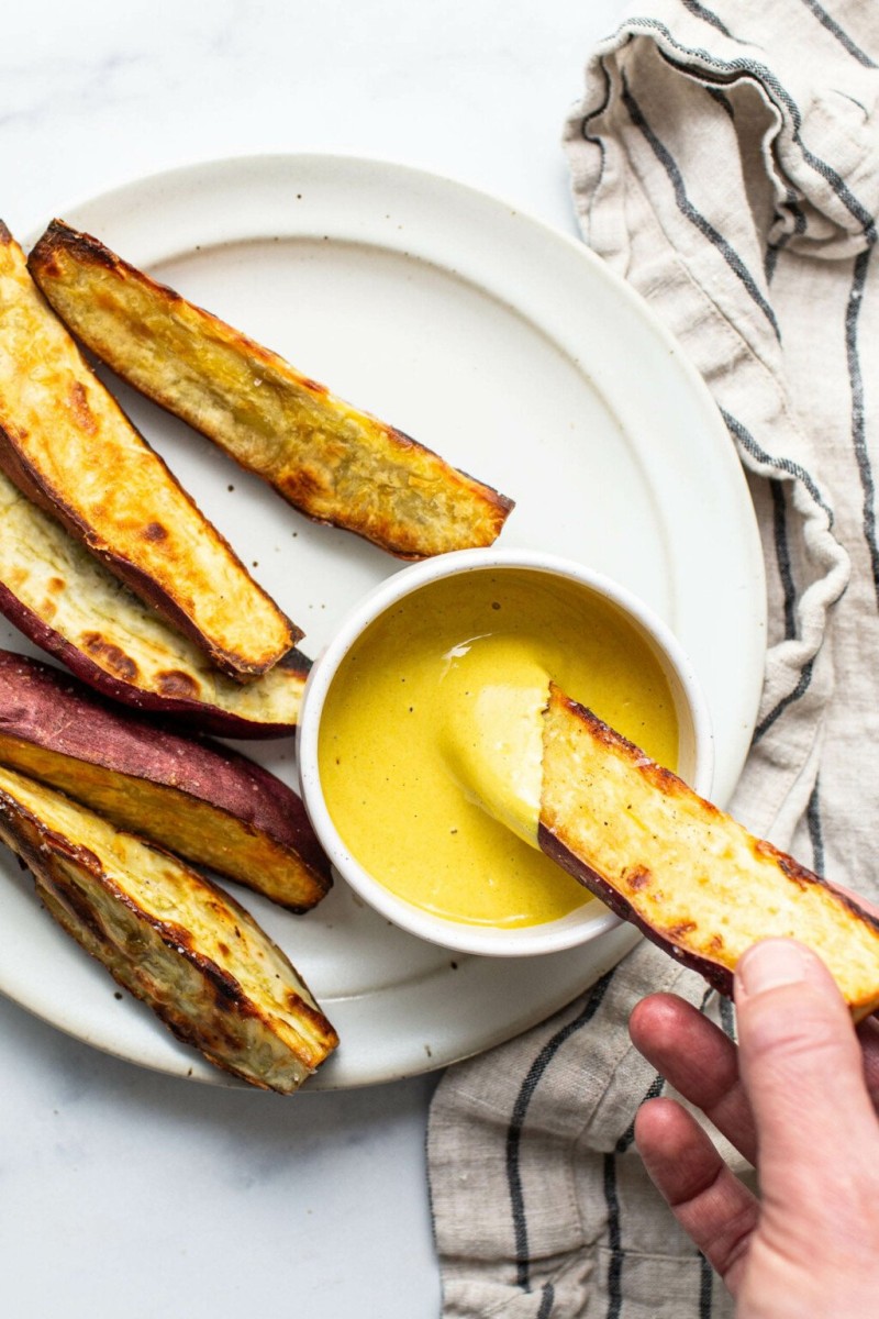 An overhead image of crispy roasted Japanese sweet potato wedges. They're arranged on a white platter with a bright yellow dipping sauce.