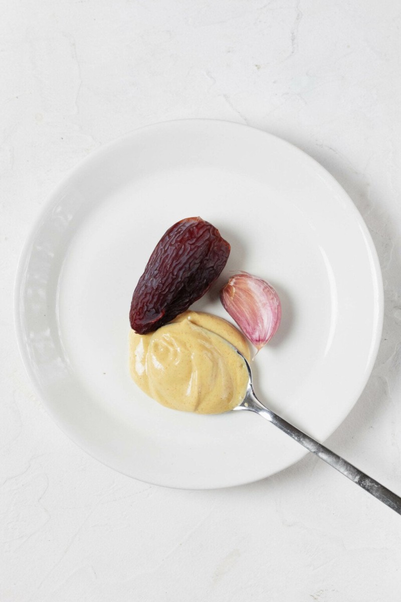 An overhead image of a small serving plate with a pitted date, mustard, and shallot.